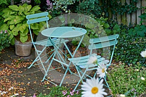 Chairs and a table with blossoming plants in a park or private patio outdoors. Empty seating in a lush green garden to