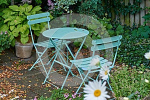 Chairs and a table with blossoming plants in a park or private patio outdoors. Empty seating in a lush green garden to photo