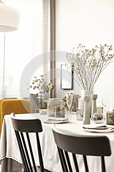 Chairs and table with flower and tableware in a dining room interior. Real photo