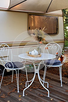 Chairs and table with tea set placed outside cozy retro caravan trailer on lawn. Interior cozy wooden RV house porch with garden f