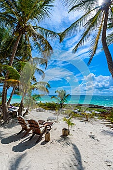 Chairs under the palm trees on paradise beach at tropical Resort. Riviera Maya - Caribbean coast at Tulum in Quintana Roo, Mexico