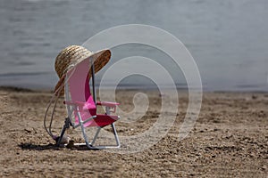 Chaise longue with straw hat on the back on a beach near waterline