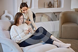 Chaise longue with two sisters with phone on sofa.