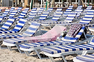 Chaise lounges with blue mattresses stand on the sand on the beach, one chaise longue is occupied