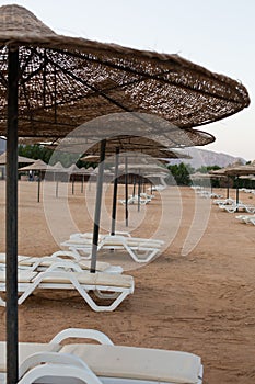 Chaise lounges and straw umbrellas at empty evening beach