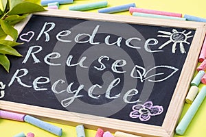 Chalk board Reduse Reuse Recycle sign on a yellow background with green leaves and chalk pieces