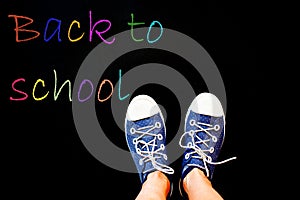 chalk and kid& x27;s feet on black background wearing sneakers - back to school concept
