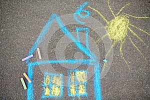 Chalk picture of house and sun on asphalt of sidewalk. Kids creative picture on gray background of road