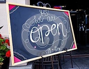 Chalk sign at resturant in welcoming artisitic cursive writing stating Yes We Are Open