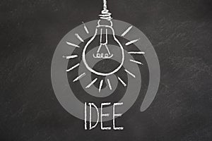 Chalk text `Idee` and lightbulb on chalkboard. Translation: `Idea`