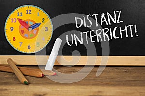 Chalkboard with clock and wooden pencils and the german words for distance learning, distance education or home schooling - distan