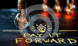 Chalkboard concept with lightbulbs and highlighted PAY IT FORWARD message, representing the idea of passing on a good deed and