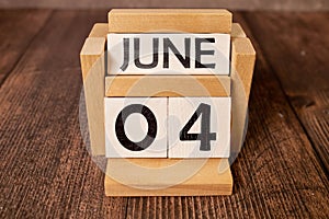 Chalkboard with June 04 calendar date on white cube block on wooden table.