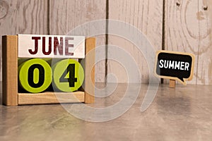 Chalkboard with June 04 calendar date on white cube block on wooden table.