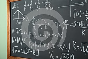 Chalkboard with many different math formulas on green wall, closeup