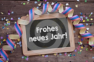 Chalkboard with paper streamers and confetti with the german words for happy new year - frohes neues jahr 2022 on wooden backgroun