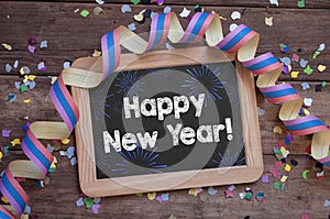 Chalkboard with paper streamers and confetti with happy new year 2022 on wooden background