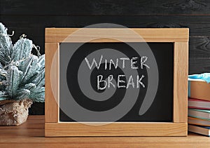 Chalkboard with phrase Winter Break, small Christmas tree and books on wooden table. Holidays concept