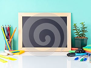 Chalkboard and school supplies on white table by the blue wall.