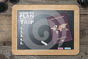 A chalkboard showing tips to plan a trip. Black chalkboard with sunglasses, lens and some coins around it and a passport showing