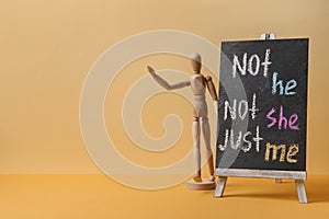 Chalkboard with text Not he, not she, just me and mannequin on pale orange background. Gender identity