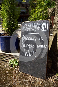 Chalkboard warning that wooden decking is slippery when wet.