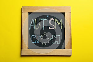 Chalkboard with word Autism and drawn jigsaw puzzle pieces on yellow background, top view