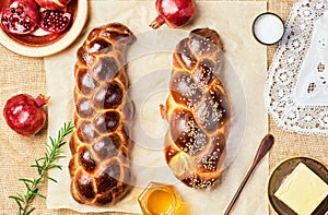 Challah bread, freshly baked sweet braided bread on parchment, sackcloth background. Pomegranates, apples, butter and honey for