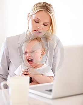 Challenges of working mothers. A businesswoman trying to work on her laptop while her baby cries.