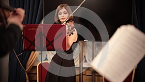 Chamber orchestra. A young beautiful woman playing violin during a performance.