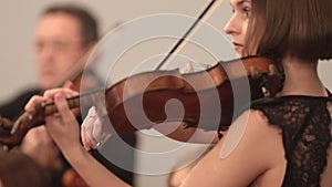 Chamber orchestra. A young woman playing violin during a performance. Side angle.