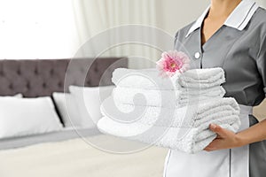 Chambermaid with stack of fresh towels in hotel room. Space for text