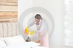 Chambermaid wiping dust from lamp in bedroom