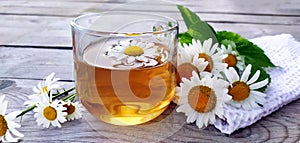 Chamomile aromatic tea close-up in a glass cup on a wooden background. Summer still life with wildflowers and medicinal herbal