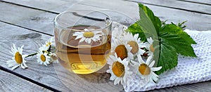 Chamomile aromatic tea in a glass cup on a wooden background. Floral banner. Summer still life with wildflowers and medicinal