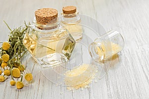 Chamomile flower water. Glass bottles with infusion or hydrolate of pharmaceutical chamomile and bath or SPA salt on wooden white