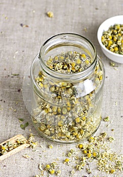 Chamomile herbal tea in chinese cup and glass jar with dry herb flowers, above overhead view