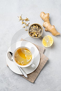 Chamomile herbal tea with lemon in a white cup on a light background with dry flowers and ginger. The concept of a healthy detox