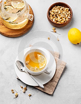 Chamomile herbal tea with lemon in a white cup and teapot with flowers on a light background. The concept of a healthy detox drink