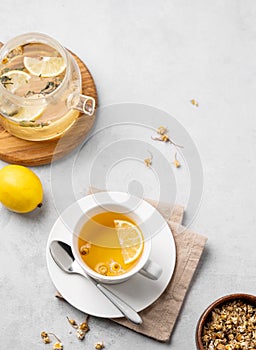 Chamomile herbal tea with lemon in a white cup and teapot with flowers on a light background. The concept of a healthy detox drink