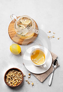 Chamomile herbal tea with lemon in a white cup and teapot with flowers on a light background. The concept of a healthy detox drink