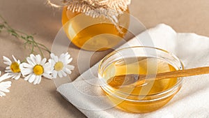 Chamomile syrup in a small bowl and in a jar and chamomile flowers on a linen kitchen towel