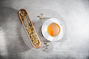 Chamomile tea cup with loose flowers or dried petals ongray table. Top view - above