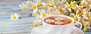 Chamomile tea, daisy flowers and a bouquet of Matricaria chamomilla on a wooden background