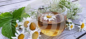 Chamomile tea in a glass cup close-up on a wooden background. Summer still life with wildflowers and medicinal chamomile drink.