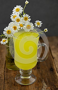 Chamomile tea in a glass cup on a wooden table. Bouquet of medicinal chamomile. Aromatherapy and herbal medicine. Daisies are