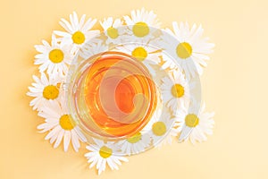 Chamomile tea in a transparent cup on a yellow background.