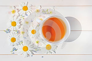 Chamomile tea in a white little cup on a light wooden surface.