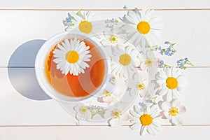 Chamomile tea in a white little cup on a light wooden surface.