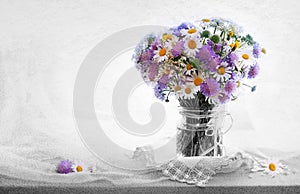 Chamomiles bouquett in vase on fabric background.